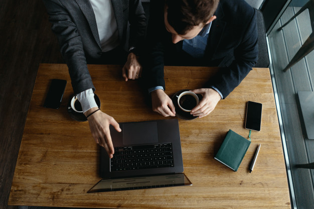 Dos hombres empresarios en asesoría internacional, mirando un portátil mientras toman café