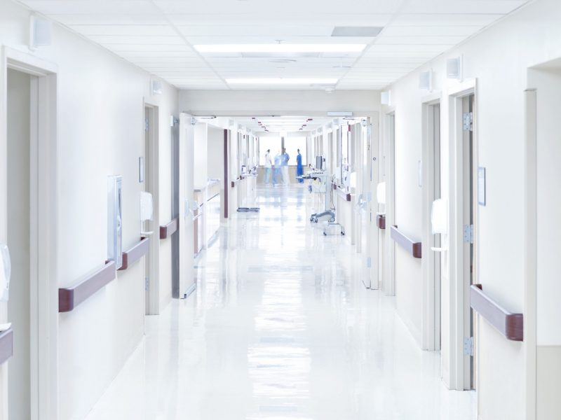 Pasillo blanco de hospital, con varios enfermeros vestidos de azul al fondo